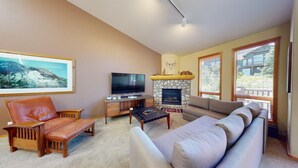 A living room with a stone fireplace, a television, a sofa, a leather chair, and a framed picture on the wall. - Snowcreek Resort Vacation Rental 950 (Mammoth Lakes)