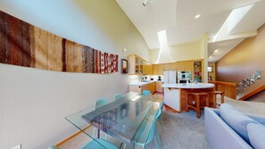 Een modern interieur met een glazen eettafel, houten kasten en een keukenhoek.