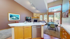 A modern kitchen with a central island, a flat-screen TV, and a stone fireplace.