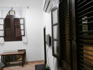 A room with a wooden table, a TV mounted on the wall, and a window with wooden shutters. - Apto Havana Center Home (Havana)