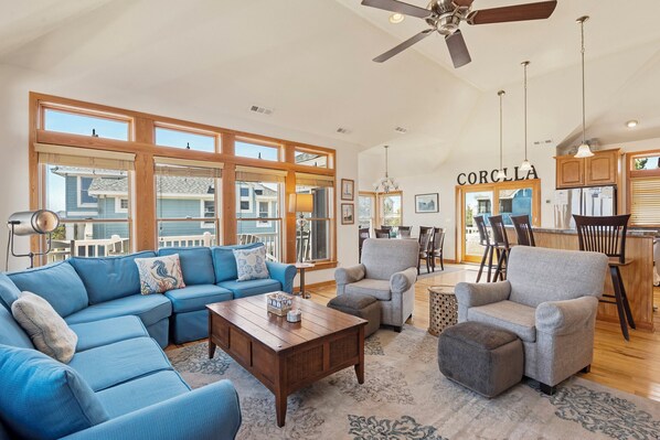 A spacious living room with a sectional sofa, armchairs, a coffee table, and a dining area with a kitchen in the background.