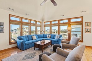 Ein geräumiges Wohnzimmer mit einer großen Eckcouch, einem Couchtisch und Sesseln. Große Fenster bieten einen Ausblick nach draußen.