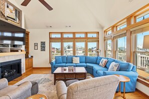 A living room with a blue sectional sofa, a fireplace, and large windows with a view of houses.