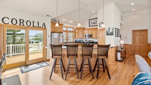 Una cocina amplia con gabinetes de madera, una isla central con taburetes altos y un ventanal corredizo que da a un balcón.