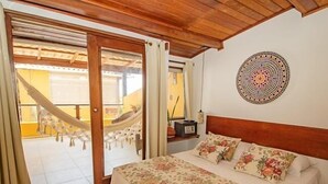 A bedroom with a bed, a hammock, and a view of a yellow building. - Pousada Funny (Cairu)