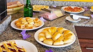 A buffet table with various food items, a green bottle, and hanging plants. - Pousada Funny (Cairu)