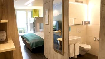 A hotel room with a bed, a bathroom with a toilet and sink, and a wooden shelf with towels.