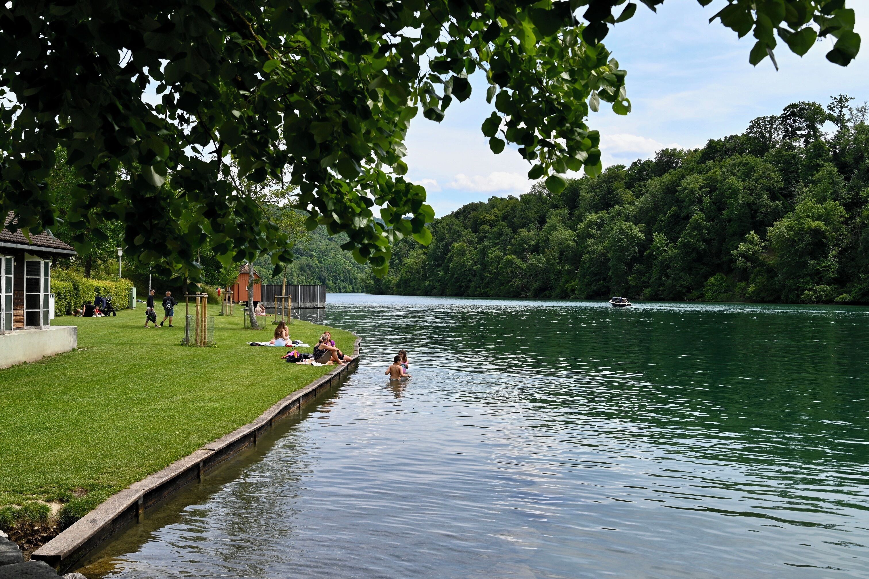 Um parque à beira do lago com gramado, um píer de madeira e um barco na água.