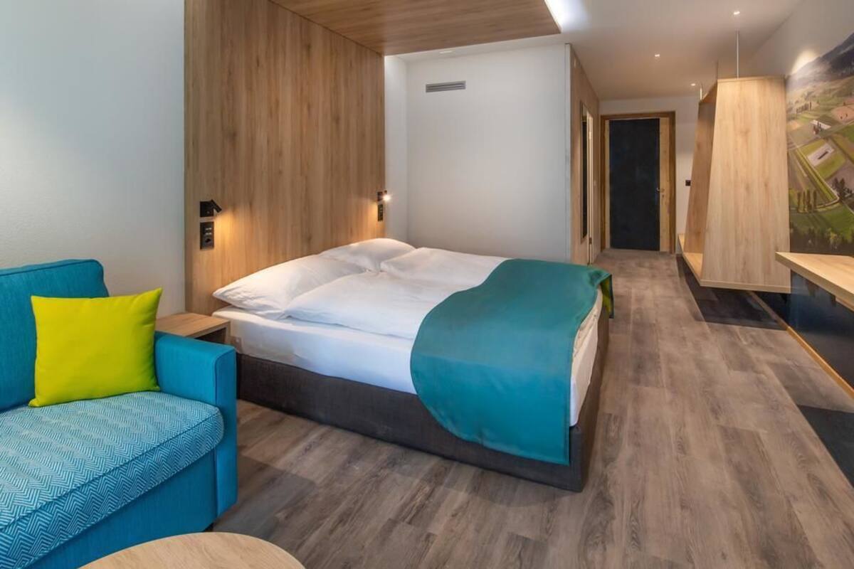A modern hotel room with a bed, a blue sofa, and a wooden accent wall.