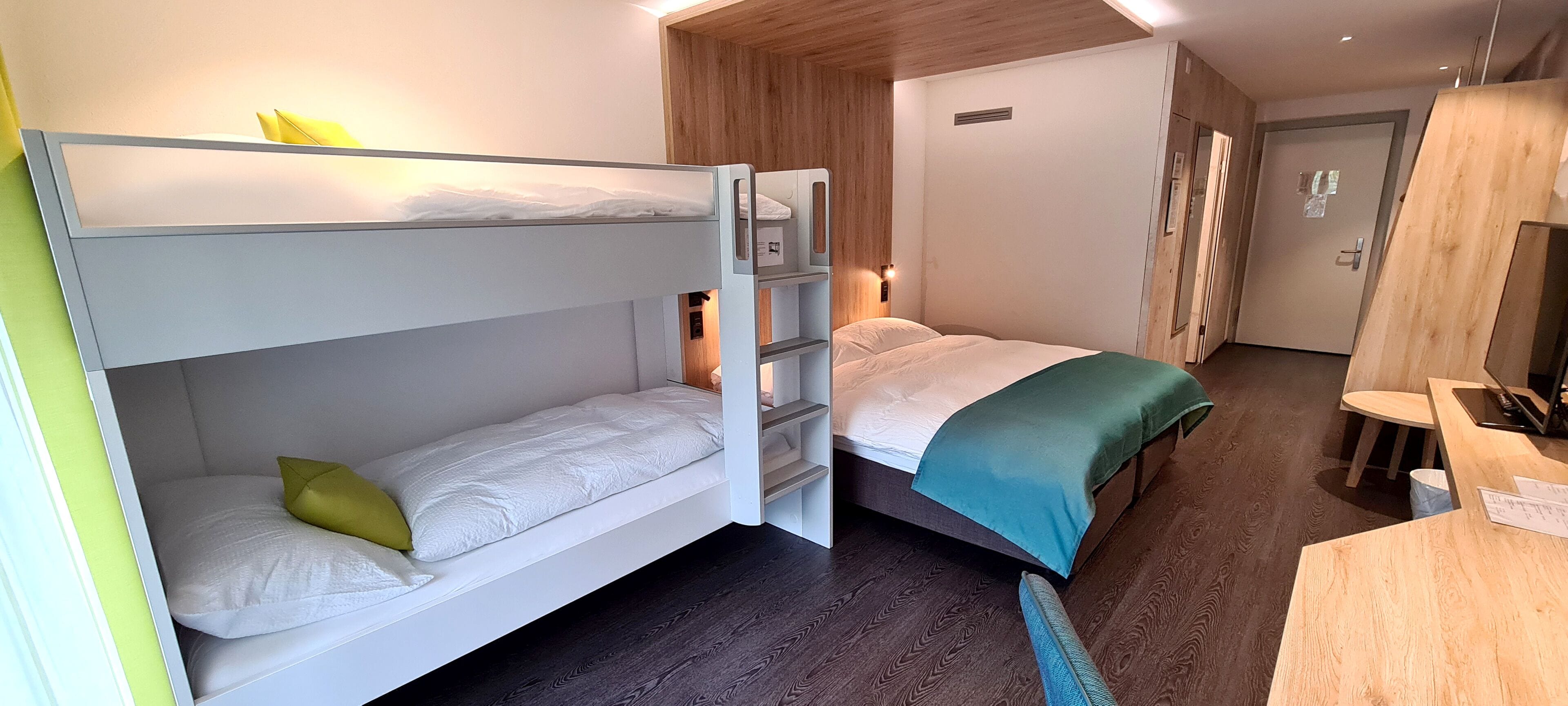 A bunk bed room with a desk and a wardrobe.