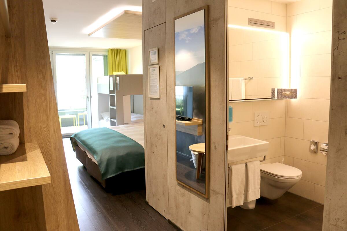 A hotel room with a bed, a bathroom with a toilet and sink, and a wooden door.
