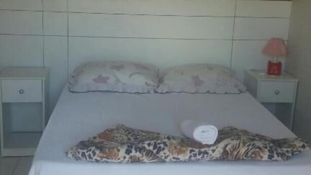 A neatly made bed with a patterned pillow and a white bedsheet. There are two bedside tables with lamps, one on each side of the bed. - Pousada Porto Brasil (Pocoes)