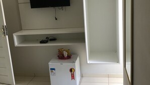 A room with a flat-screen TV mounted on the wall, a small refrigerator, and a white cabinet with open shelves. - Pousada Porto Brasil (Pocoes)