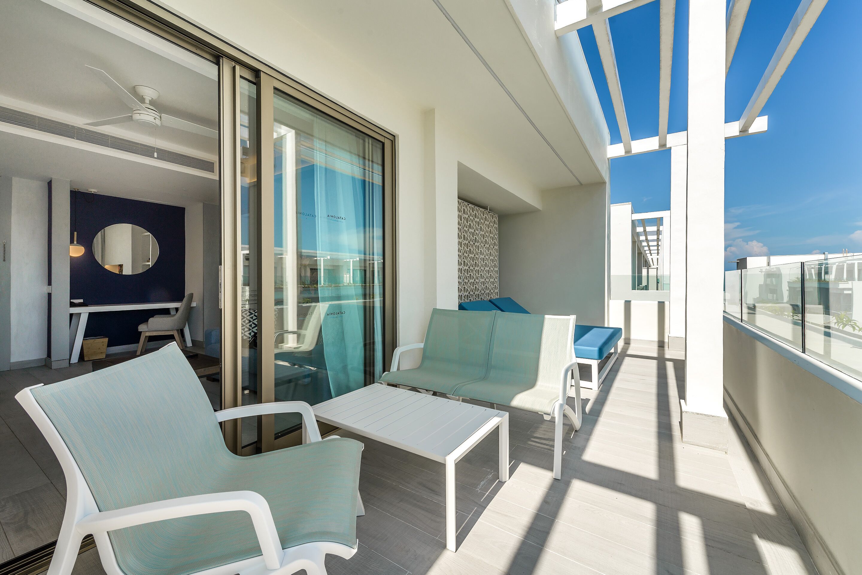 A balcony with white furniture, a glass door, and a view of the sky.