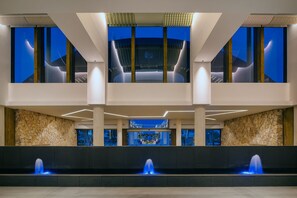 A modern lobby with a stone wall, a fountain, and a view of the sky through large windows.