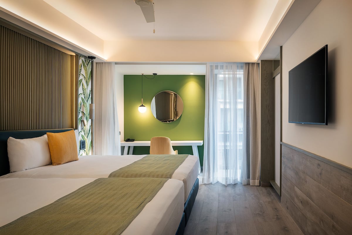 Ein Hotelzimmer mit Bett, Schreibtisch, Stuhl, Fernseher und Blick ins Freie.