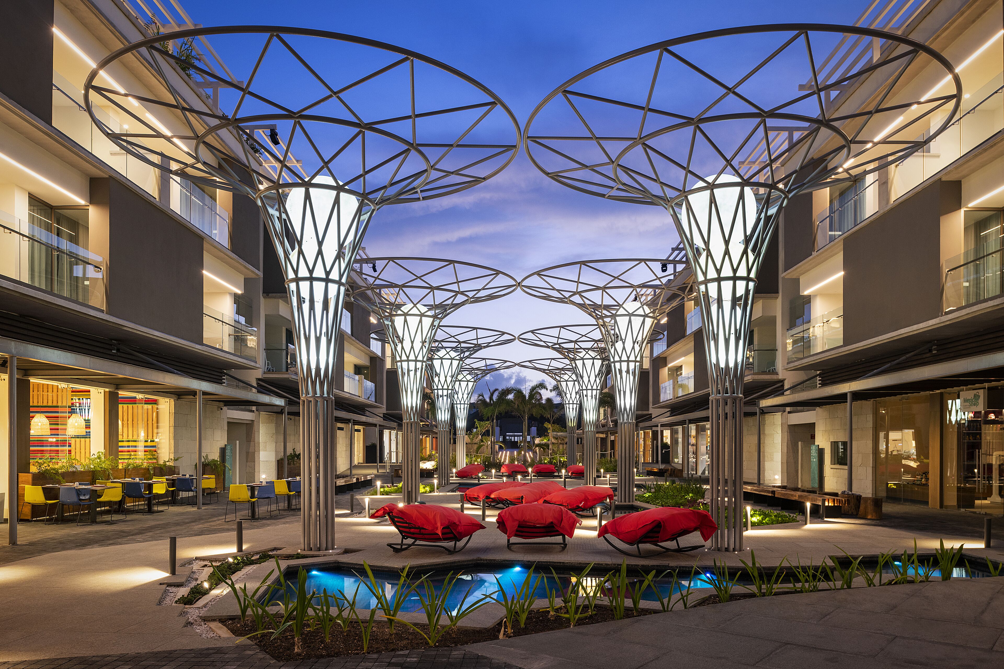 A modern hotel atrium with a pool, outdoor seating, and a unique geometric ceiling design.