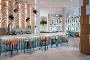 A modern bar area with a zigzag patterned wall, bar stools, and a variety of bottles.