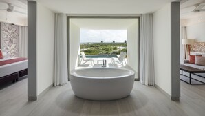 A modern bathroom with a large bathtub, a view of a pool and greenery, and a minimalist design. - Catalonia Grand Costa Mujeres All Suites & Spa - All Inclusive (Costa Mujeres)