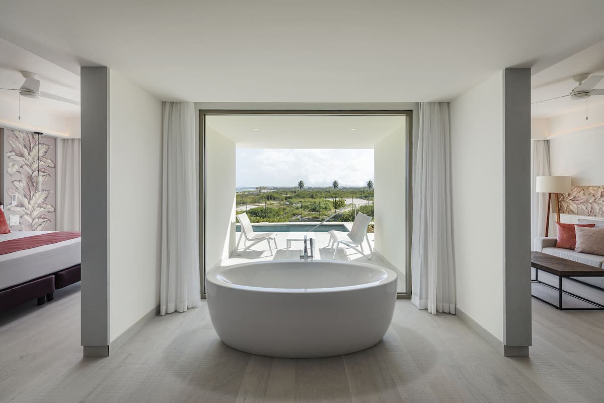 Ein modernes Badezimmer mit einer großen Badewanne, Blick auf einen Pool und Grünflächen, und minimalistischem Design.