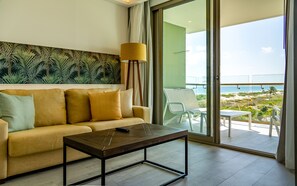 A modern living room with a sofa, a coffee table, and a view of the beach through a glass door.