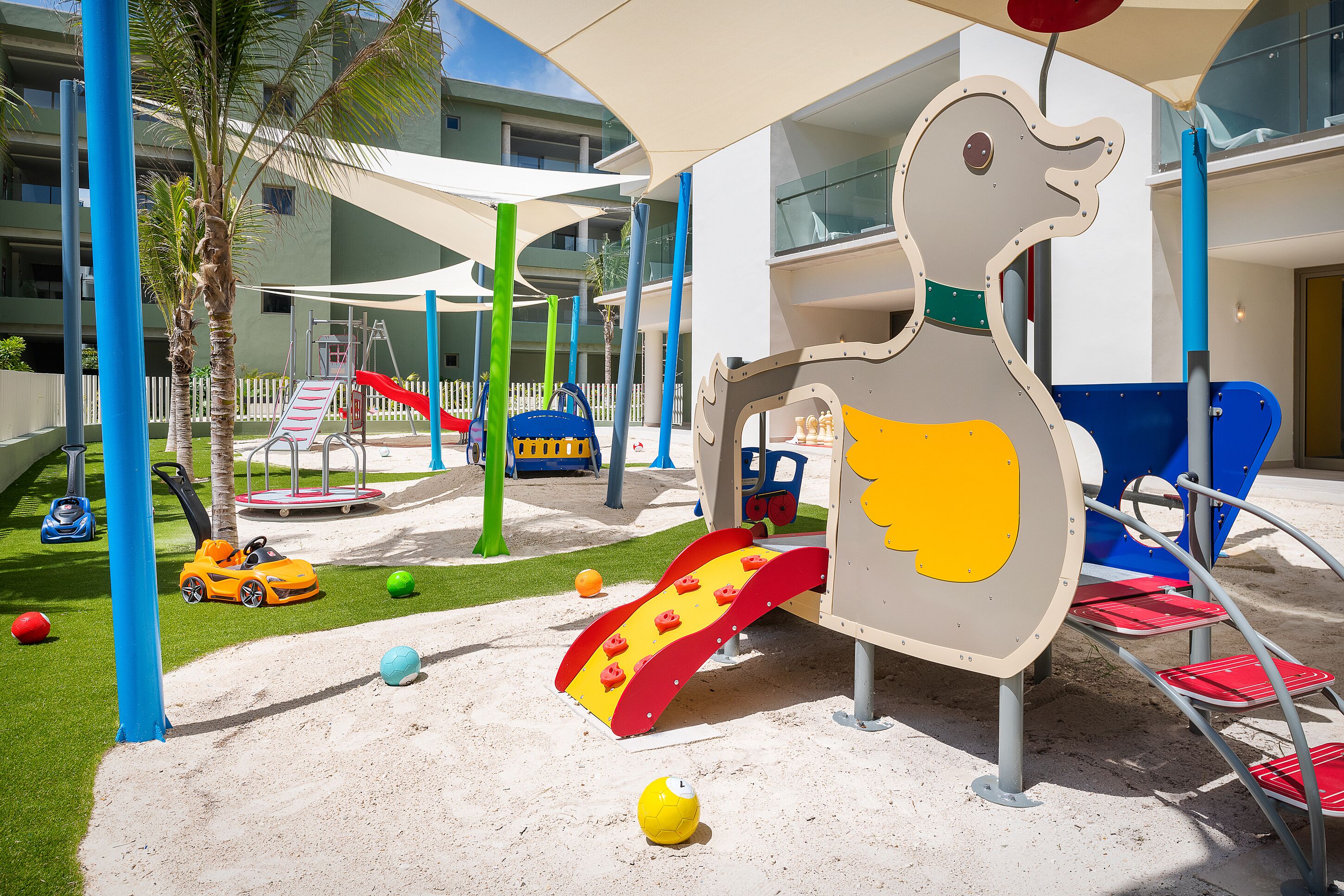 Zona de juegos infantiles con un tobogán, estructuras para escalar y una gran estructura de juego con forma de ave.
