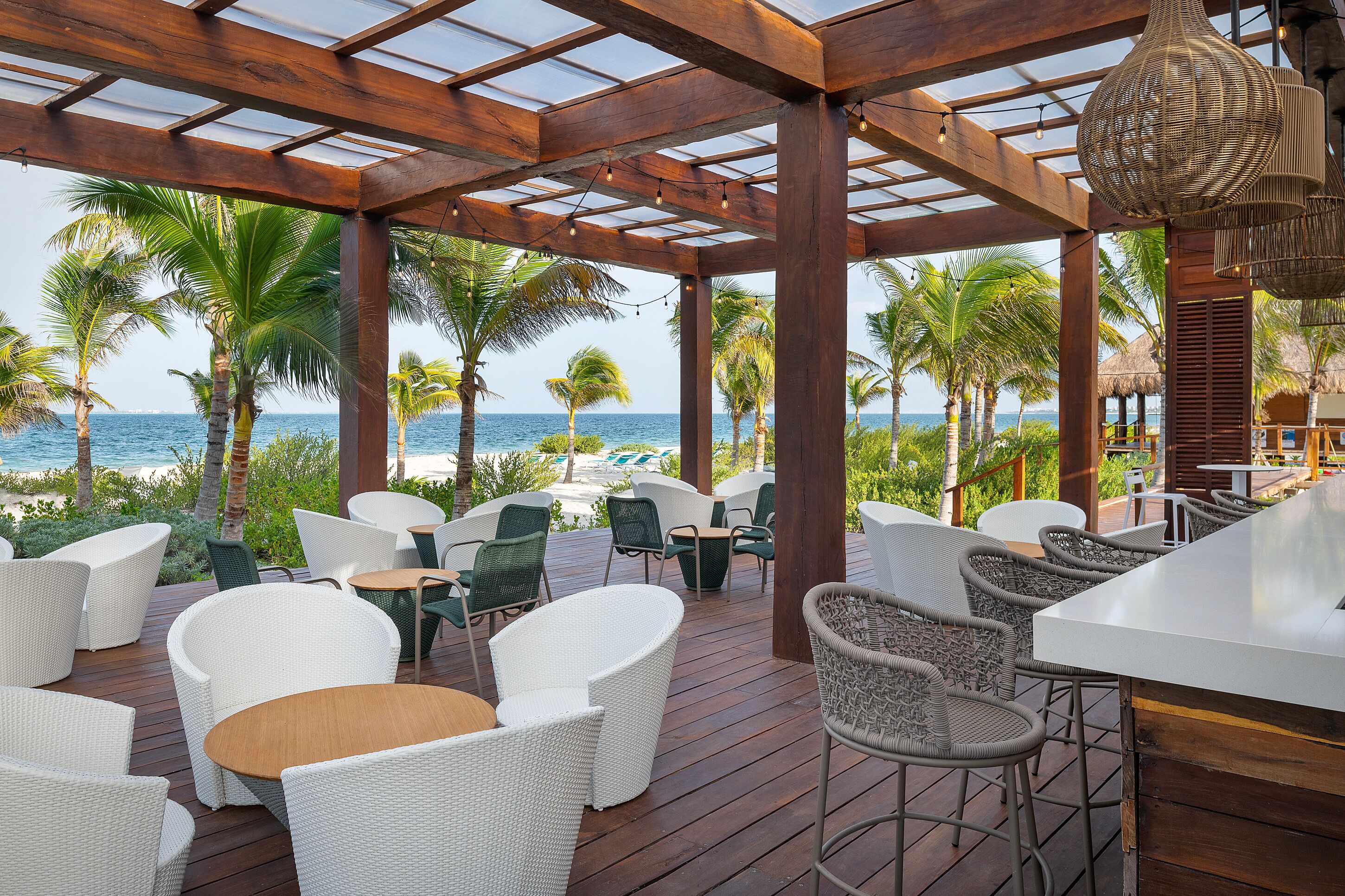 A covered outdoor seating area with wicker furniture, overlooking the ocean.