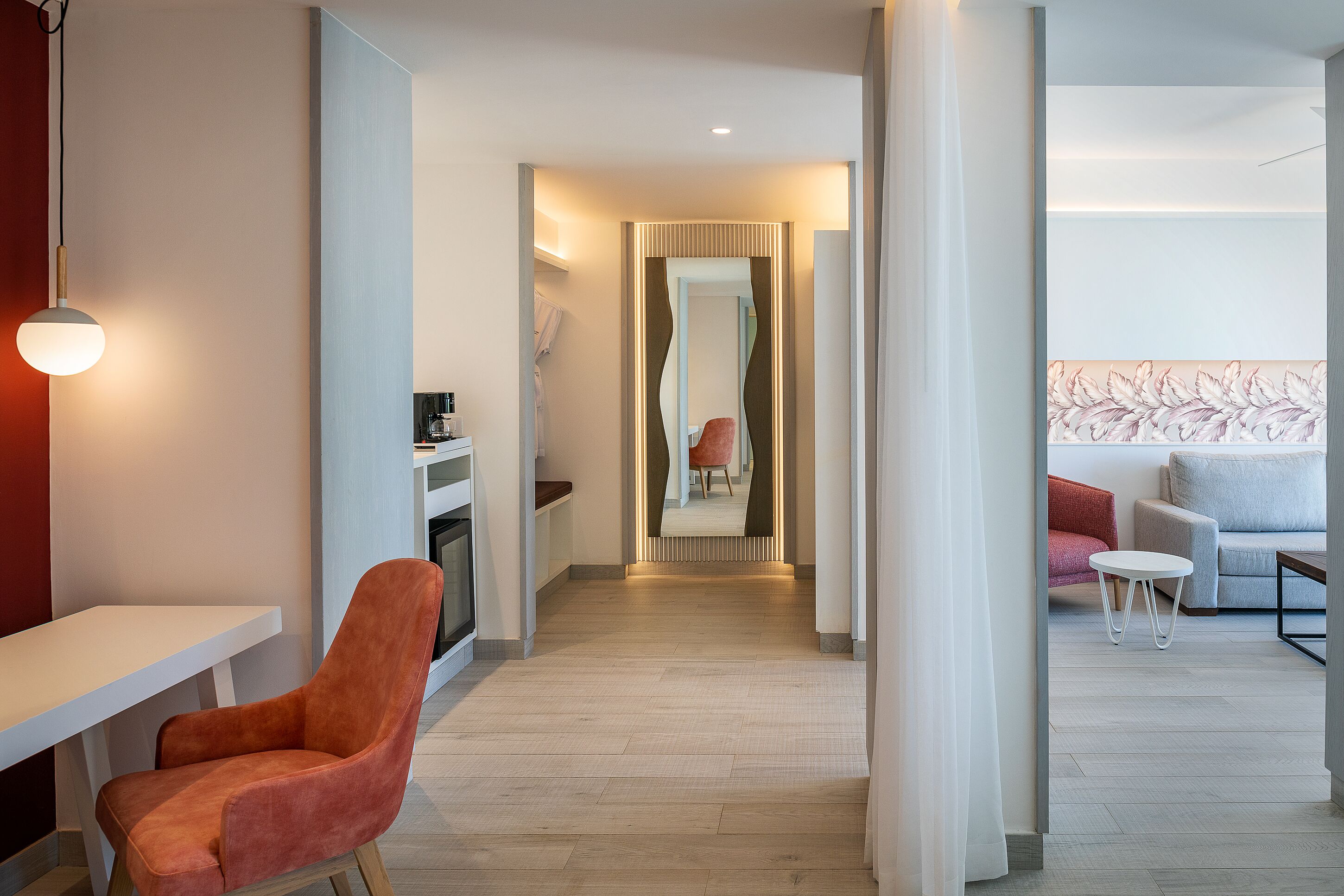 Een moderne hotelkamer met een houten vloer, een rode stoel, een witte tafel, een bank en een klein witte tafeltje.
