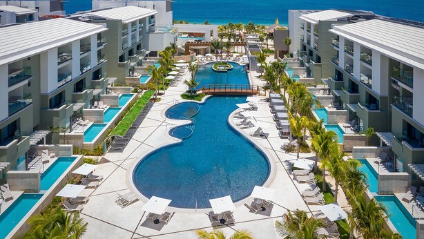 A resort with multiple swimming pools, including a central pool with a unique design, surrounded by lounge areas and palm trees. - Catalonia Grand Costa Mujeres All Suites & Spa - All Inclusive (Costa Mujeres)