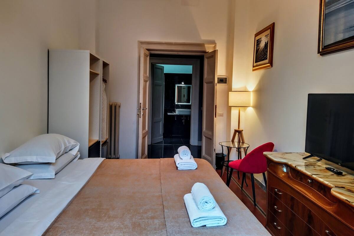 A hotel room with a bed, a desk, a chair, a TV, and a lamp.