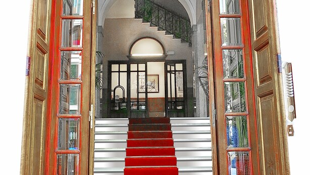 A grand staircase leading to a room with a large arched window and a view of the street below. - NIK King Rooms (Rome)