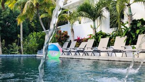 A swimming pool with water fountains, lounge chairs, and tropical plants.