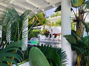Un espacio al aire libre techado con piscina, sillas de descanso y plantas tropicales.