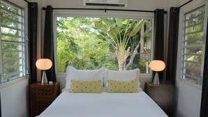 A bedroom with a large bed, two bedside lamps, and a view of greenery through the window.
