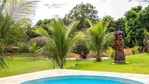 Une piscine bordée de pierres, entourée d’une végétation luxuriante et ornée d’une statue.