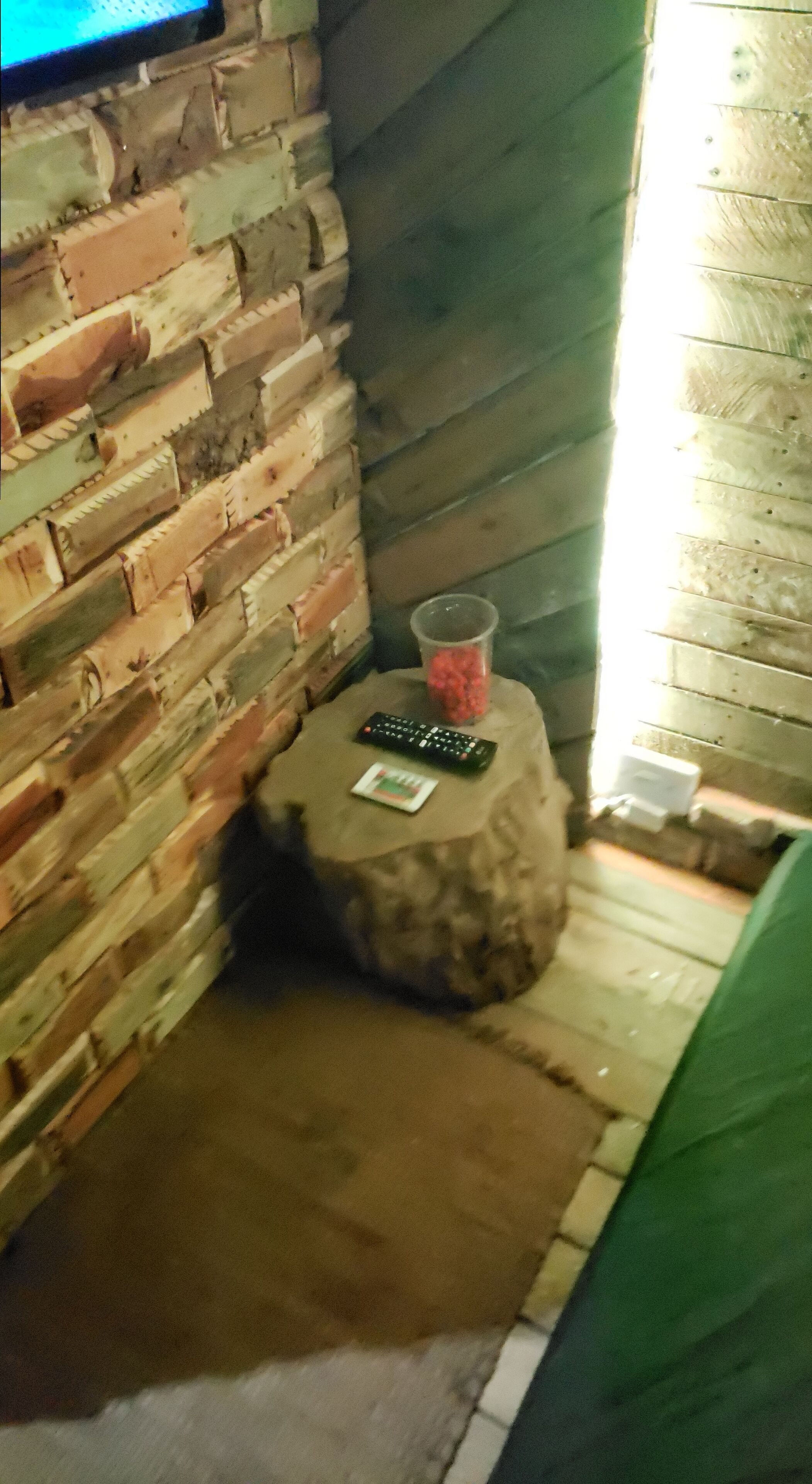 A corner with a brick wall, a small round table with a remote control, and a plastic cup.