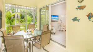 Un coin repas avec une table en verre, des chaises en osier et une vue sur la végétation tropicale, grâce à de grandes fenêtres.