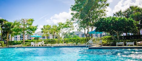 A clear blue pool surrounded by trees and buildings.