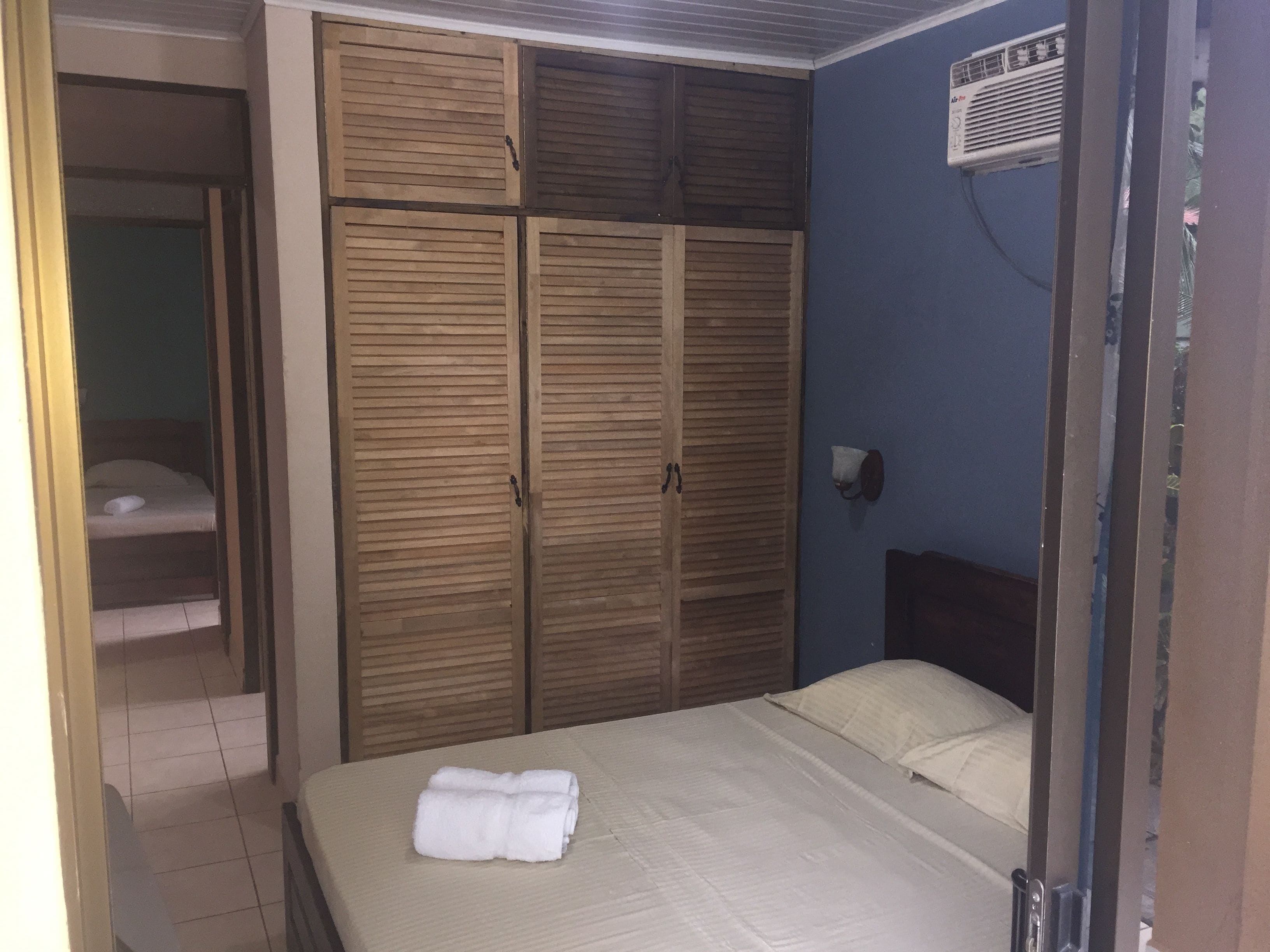 A bedroom with a bed, a wooden wardrobe, and a wall-mounted air conditioning unit.