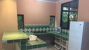 Une cuisine avec des carreaux verts et beiges, un réfrigérateur blanc et une fenêtre donnant sur un paysage verdoyant.