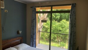 Une chambre d’hôtel avec un lit, une table de chevet, une lampe et une vue sur la verdure grâce à une grande fenêtre.