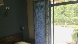 Une chambre à coucher avec un lit, une fenêtre avec des rideaux et une vue sur la verdure.