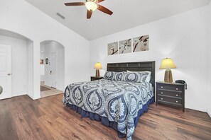 A bedroom with a bed, two bedside tables, a ceiling fan, and a door leading to another room. - 6 miles to WDW: 4 Bedroom/3+ Bath, Private Pool/Hot Tub, Wifi, Game Room, Clean (Kissimmee)