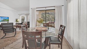 A modern living room with a glass dining table, comfortable seating, a large window with curtains, and a flat-screen TV. - 6 miles to WDW: 4 Bedroom/3+ Bath, Private Pool/Hot Tub, Wifi, Game Room, Clean (Kissimmee)