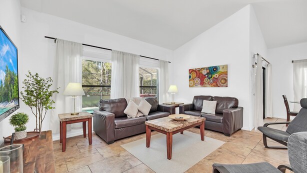 A spacious living room with a large window, a sofa set, a coffee table, and a TV. - 6 miles to WDW: 4 Bedroom/3+ Bath, Private Pool/Hot Tub, Wifi, Game Room, Clean (Kissimmee)