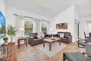 Ein geräumiges Wohnzimmer mit großem Fenster, einer Sofagarnitur, einem Couchtisch und einem Fernseher.