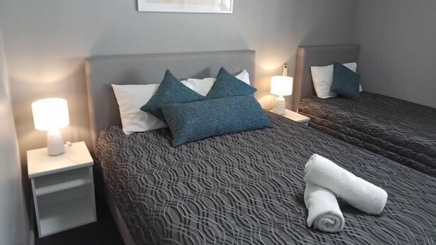 Une chambre d’hôtel avec deux lits, chacun doté d’une tête de lit, de lampes de chevet et d’une serviette roulée posée sur le lit.