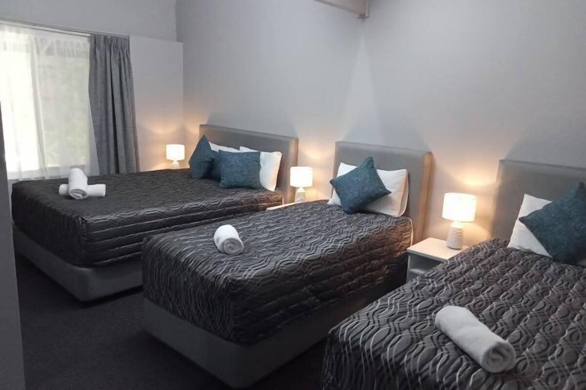 A hotel room with three beds, each with a patterned bedspread and pillows, and bedside lamps.