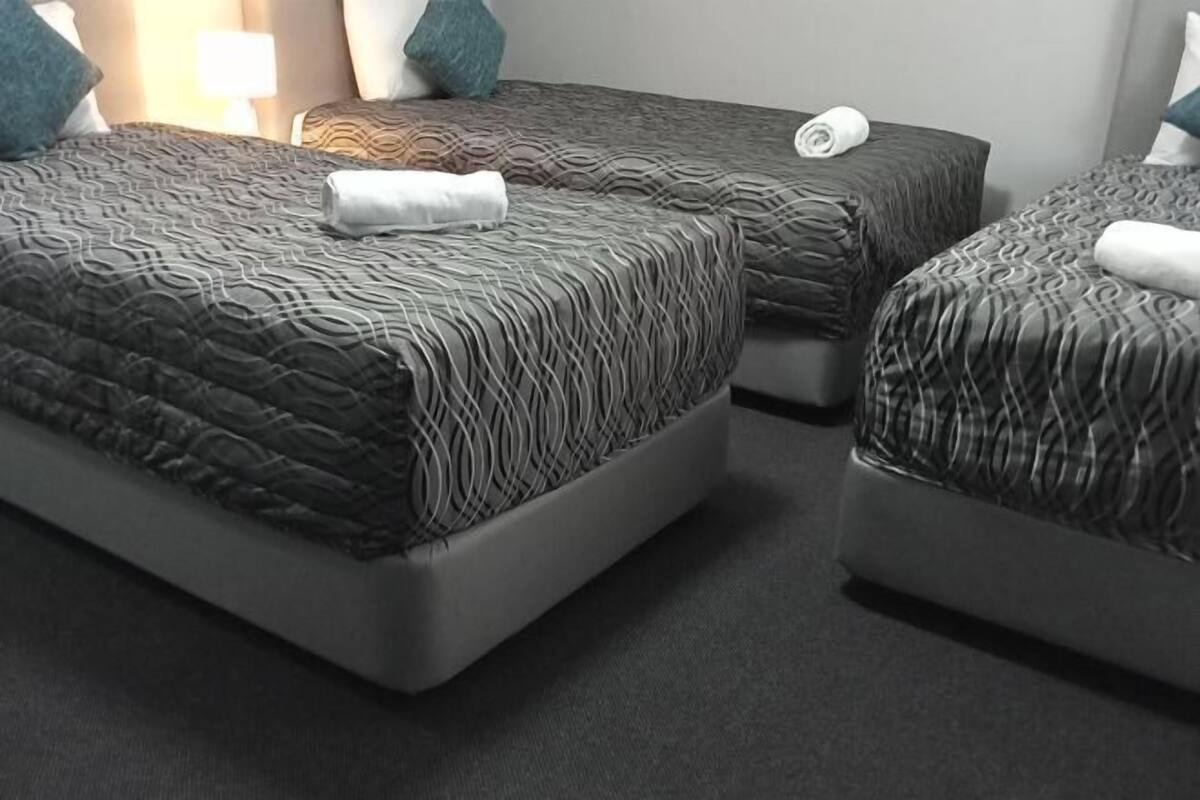 A hotel room with three beds, each with a patterned bedspread and pillows.