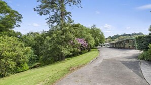 Une allée pavée mène à une série de bâtiments de style motel, avec une pelouse verdoyante et des arbres sur le côté gauche.